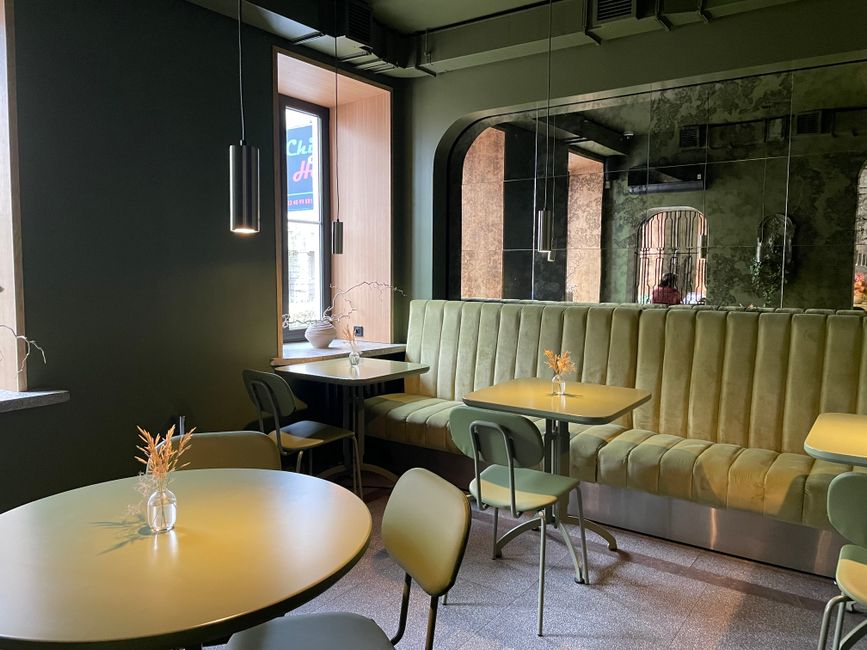 Chic cafe interior in Warsaw featuring green velvet seating and minimalist decor.