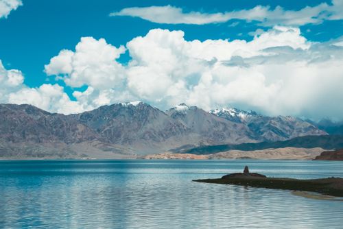 Free Tranquil mountain lake scene with dramatic clouds and snow-capped peaks. Stock Photo