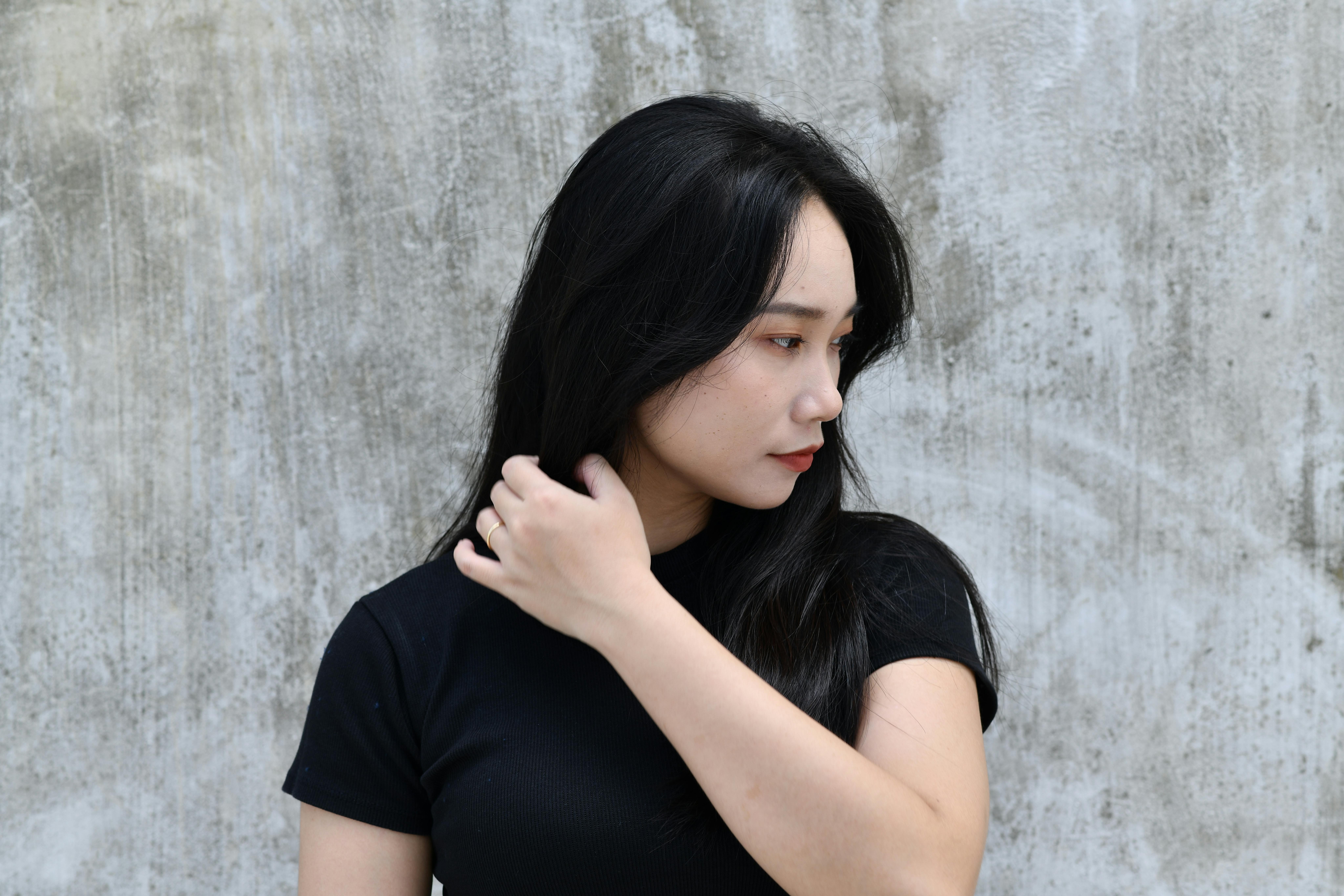 Profile of a woman with long hair touching her face in front of a concrete wall.
