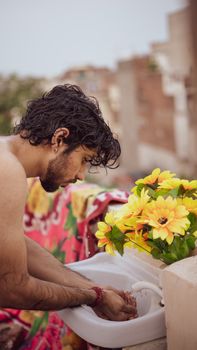 Young man washing hands in outdoor sink on rooftop, bright yellow flowers beside him.