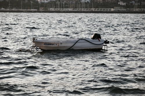 Free A solitary fishing boat named Atlantis-1 floats in the serene waters of Foça, İzmir, Türkiye at sunset. Stock Photo