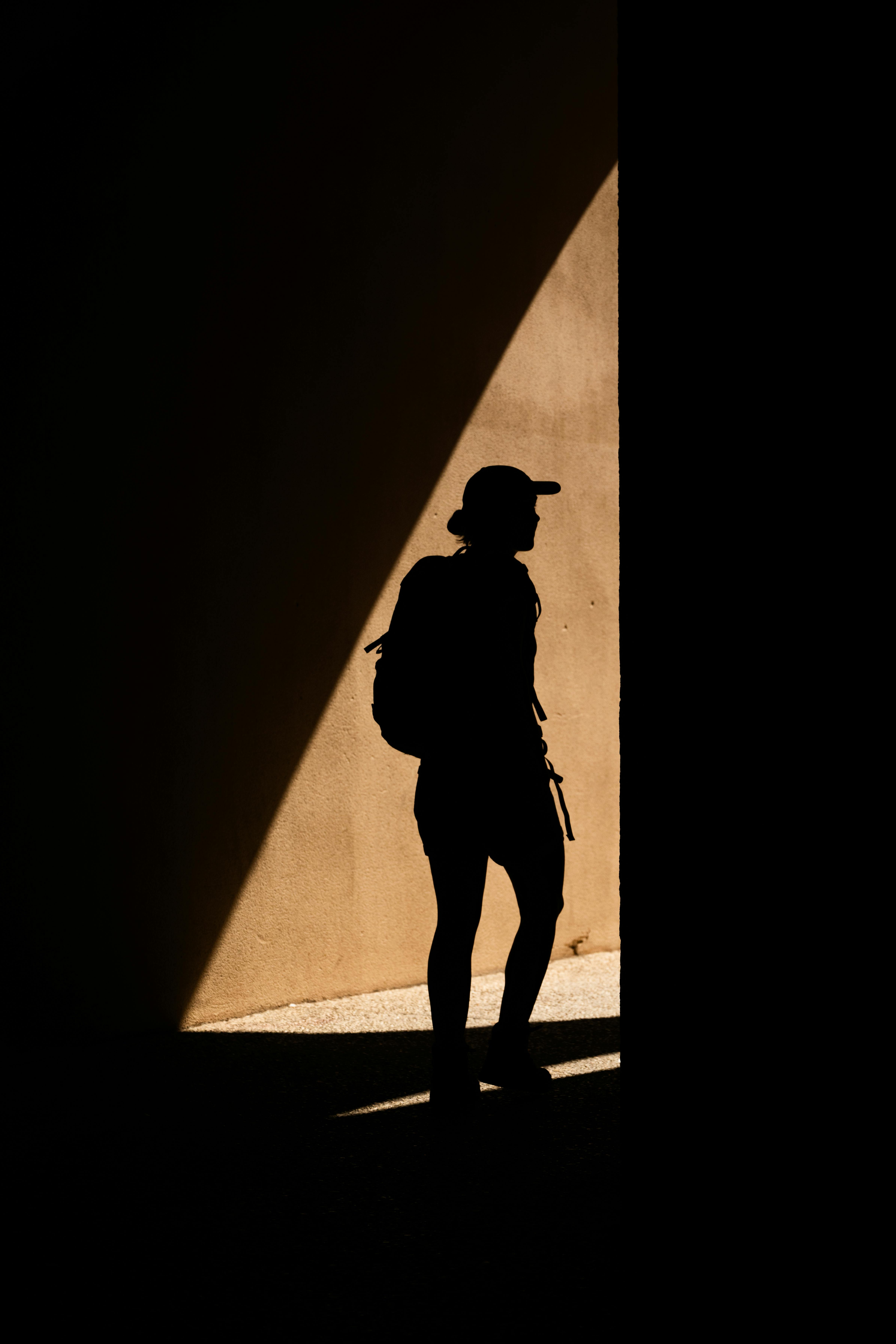 A lone traveler in silhouette against a sunlit wall in L'Isle-sur-la-Sorgue, capturing the essence of summer.