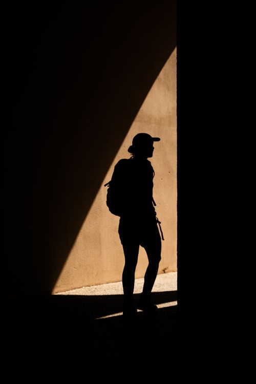 Free A lone traveler in silhouette against a sunlit wall in L'Isle-sur-la-Sorgue, capturing the essence of summer. Stock Photo