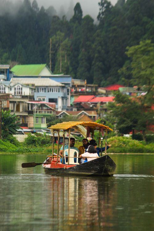 Free A wooden boat carrying passengers glides peacefully on a mountain lake with colorful houses in the background. Stock Photo
