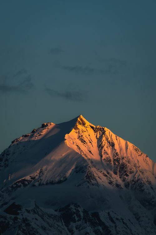 Free Sunset casts warm light on a majestic snow-covered mountain peak, capturing a serene natural scene. Stock Photo