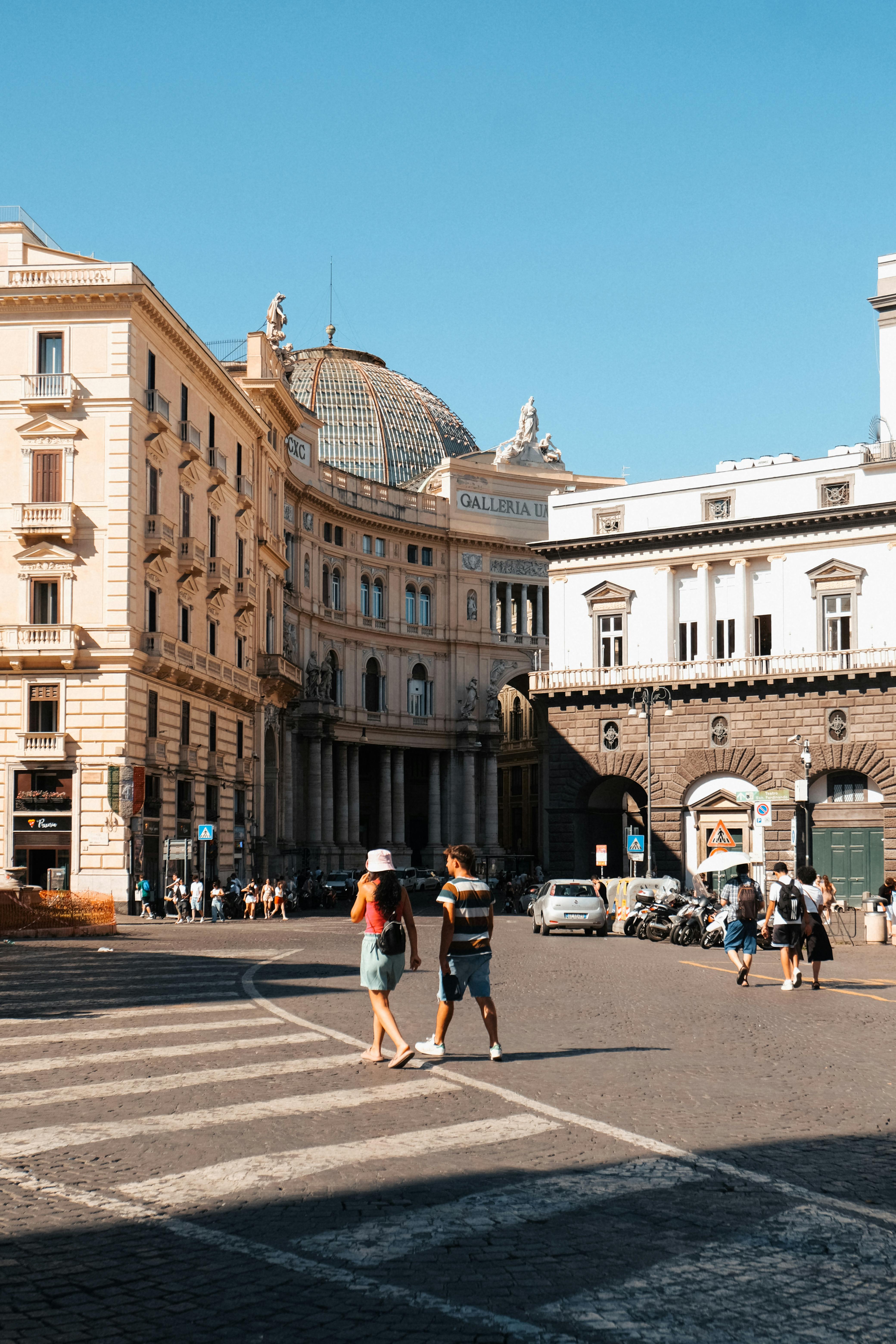 Tourists crossing street near iconic Galleria Umberto I in Naples, Italy, on a sunny day.