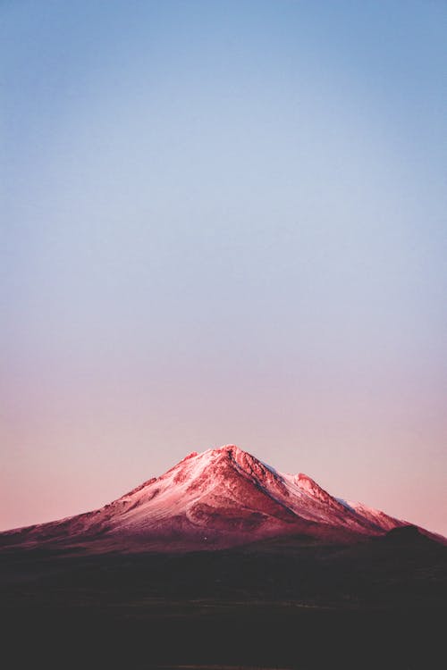 Breathtaking scenery of rough mountain peak under light purple sky during sunset