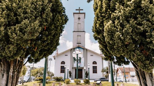 Free Serene view of a Catholic church framed by lush trees in Goiás, Brazil, during a sunny day. Stock Photo