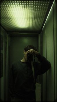 A moody self-portrait of a young man with a camera in an elevator.