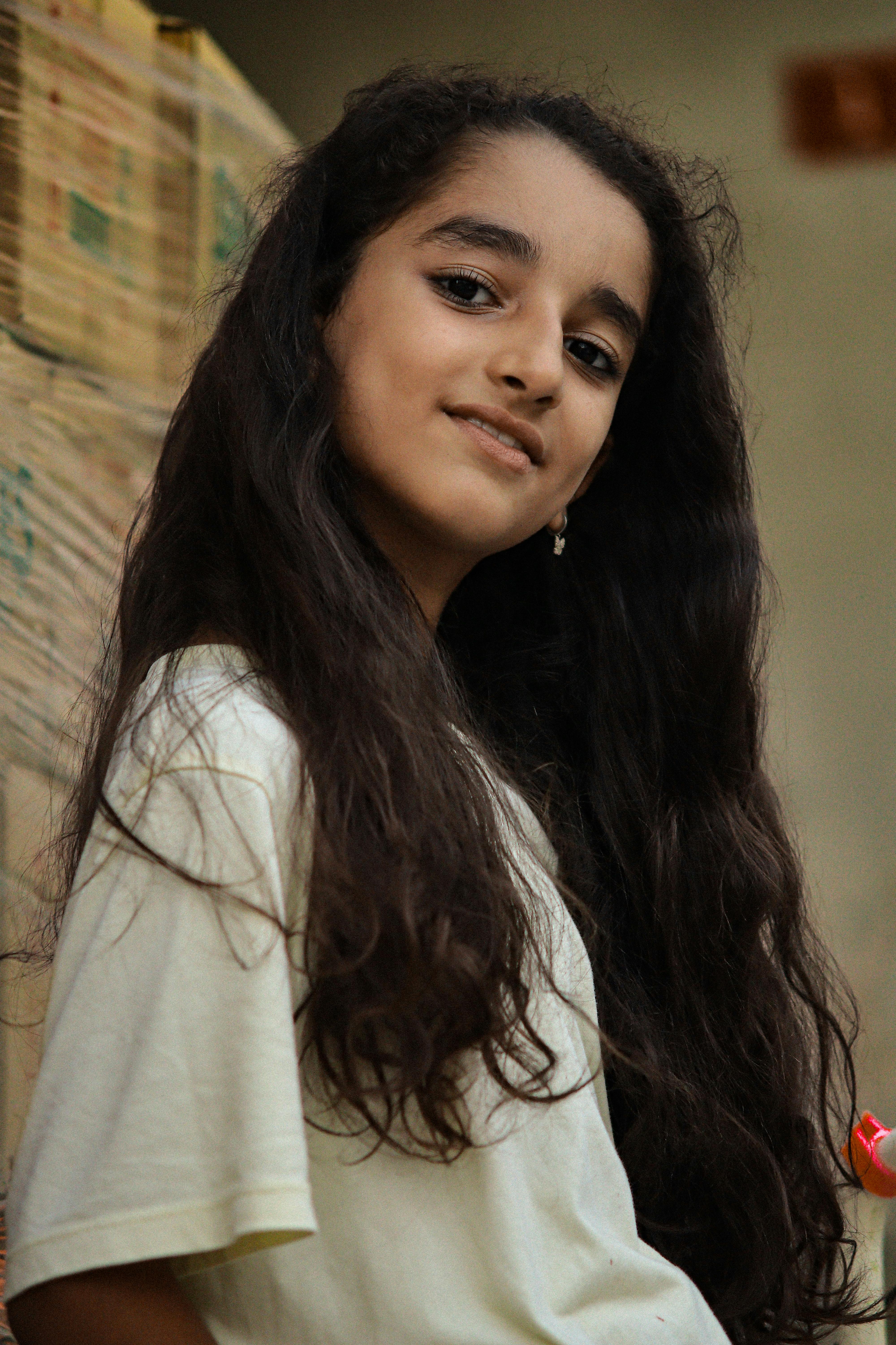 A close-up portrait of a smiling young girl with long hair indoors.