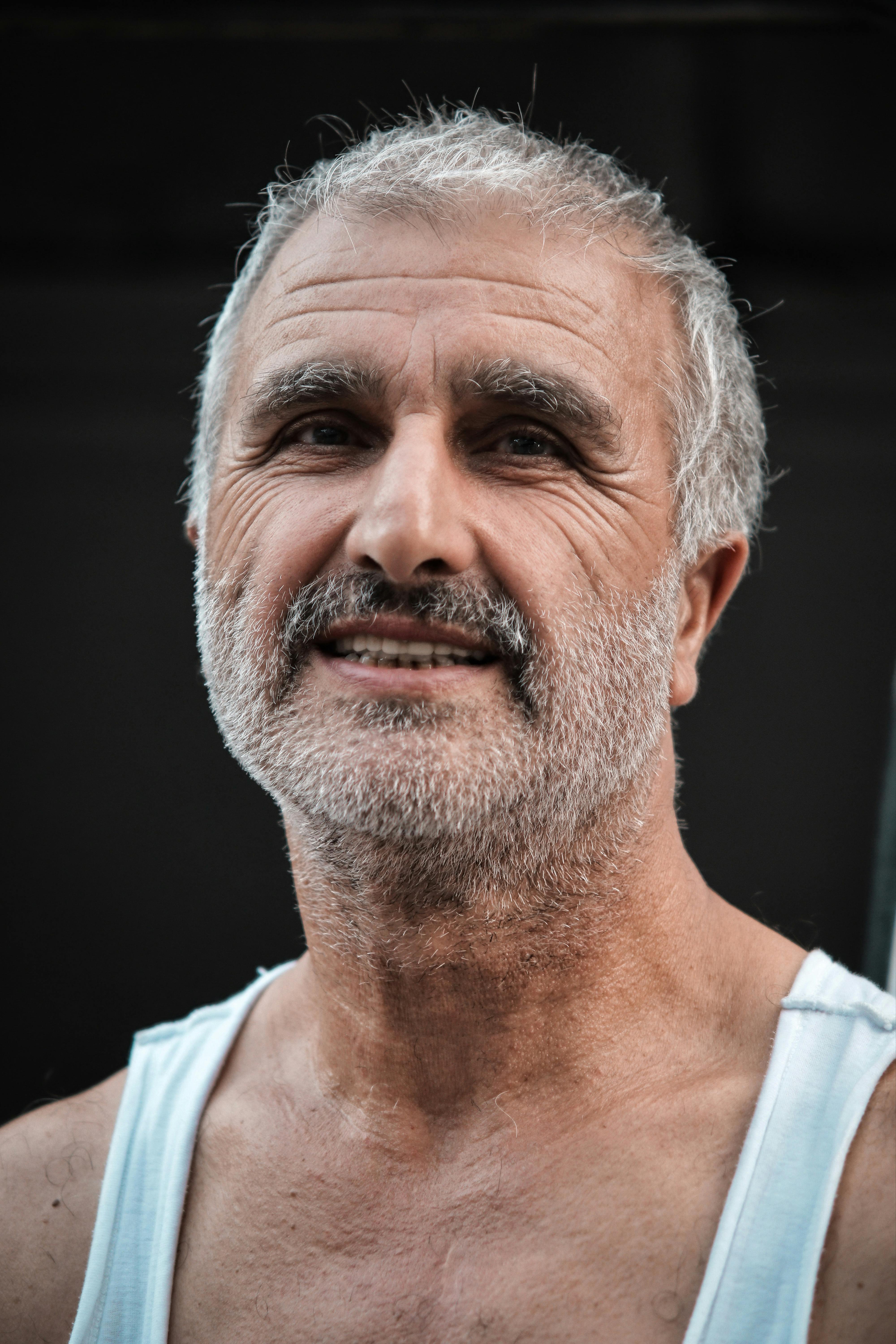 Close-up portrait of a smiling senior adult man with a beard, captured outdoors, showcasing warmth and friendliness.