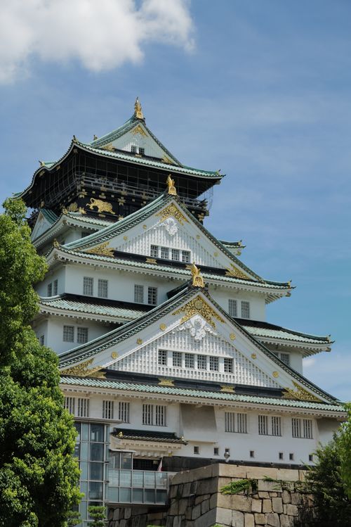 Free A majestic view of Osaka Castle with lush greenery and blue sky, a symbol of Japanese heritage. Stock Photo