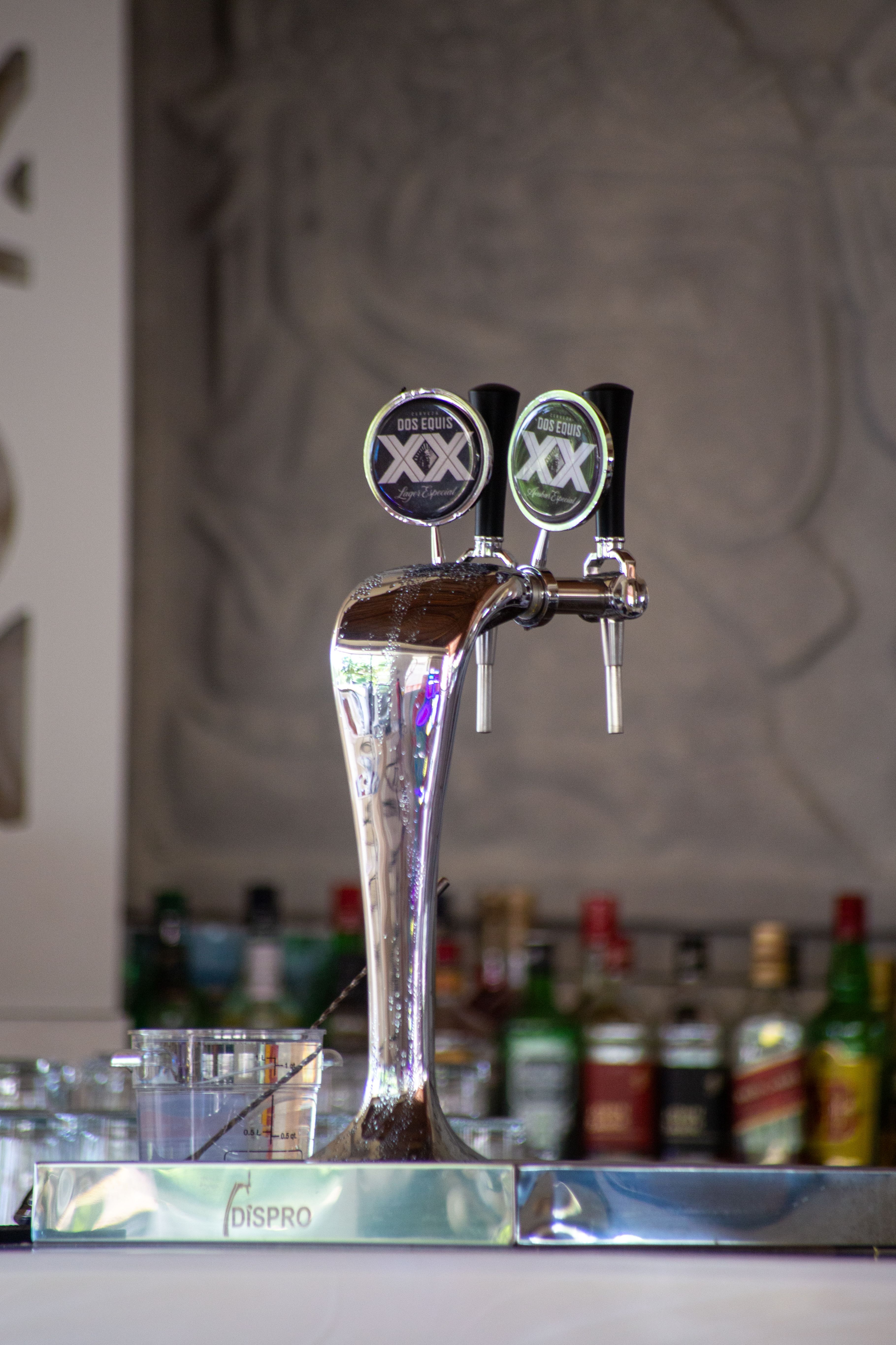Close-up of beer tap in a stylish bar setting surrounded by liquor bottles.