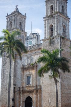 A historic Colonial-era church with twin towers surrounded by palm trees on a sunny day.