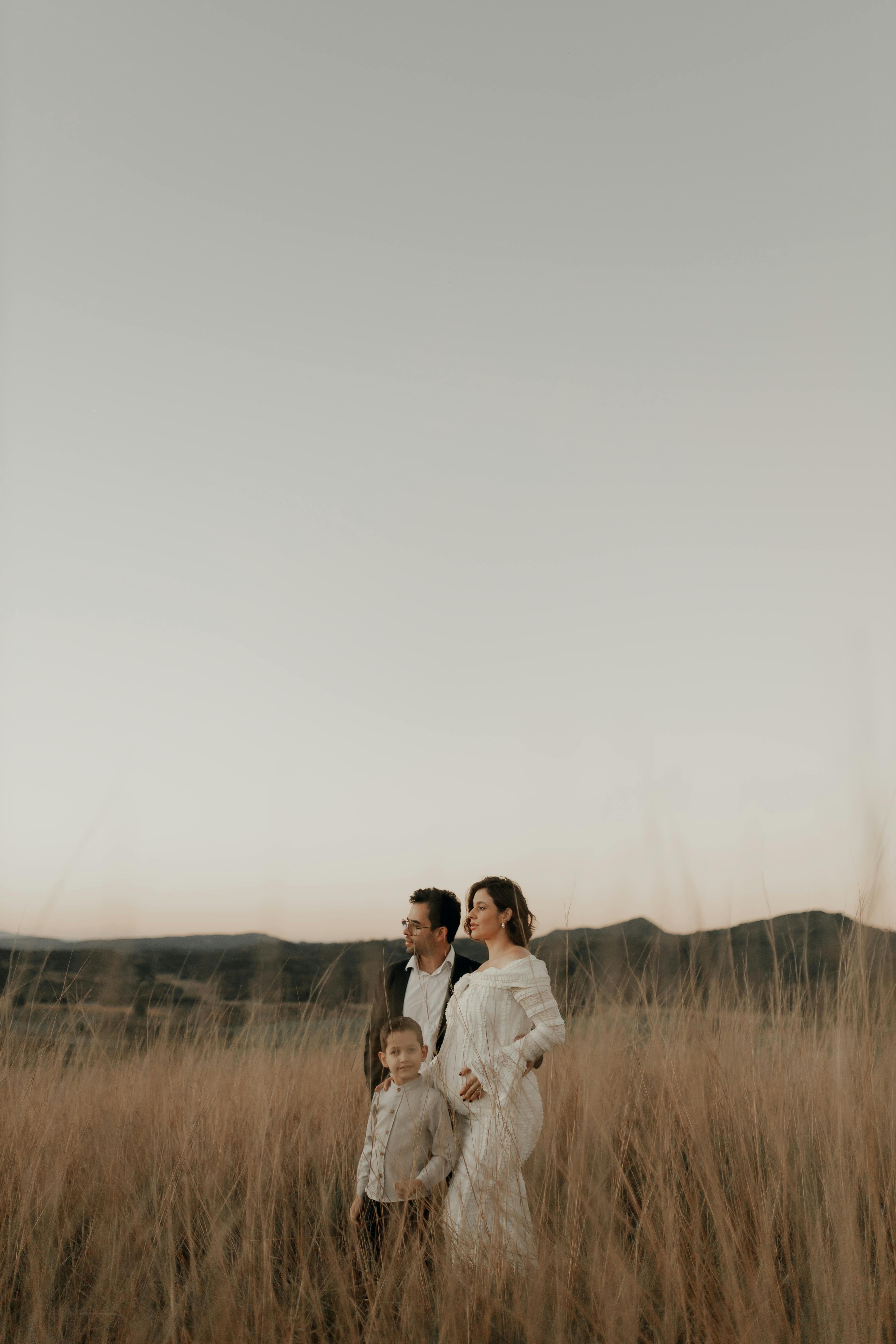 免費 一家三口在開闊的草地上欣賞著遠處群山環繞的寧靜日落。 圖庫相片