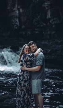 A loving couple embraces by a tranquil waterfall, capturing a moment of romance and nature.