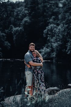 A loving couple embraces by a peaceful river, surrounded by lush greenery. Perfect for romantic themes.