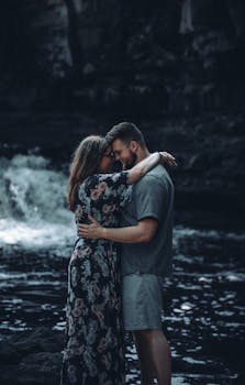 Couple embracing by a waterfall in a serene outdoor setting, exuding love and intimacy.