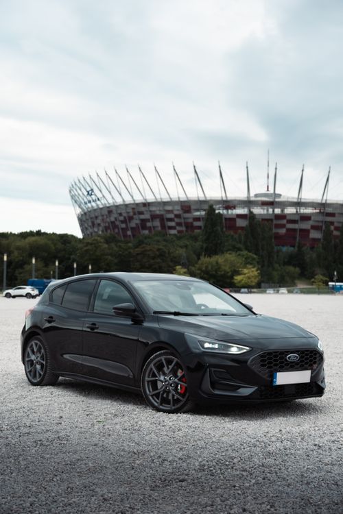 Free Black car parked in front of a modern stadium, a perfect blend of automotive and architectural design. Stock Photo
