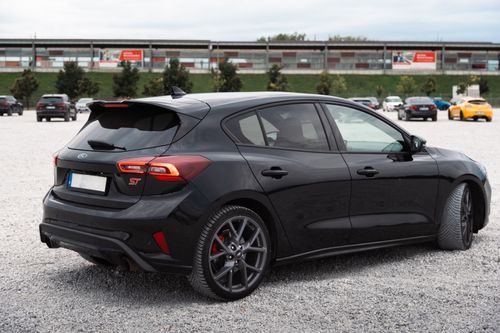 Free Modern black hatchback car parked in a spacious outdoor lot with other vehicles in view. Stock Photo