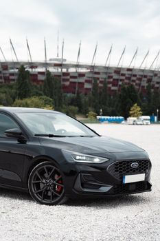 Sleek black car parked in front of a stadium during the day. Perfect for automotive themes.