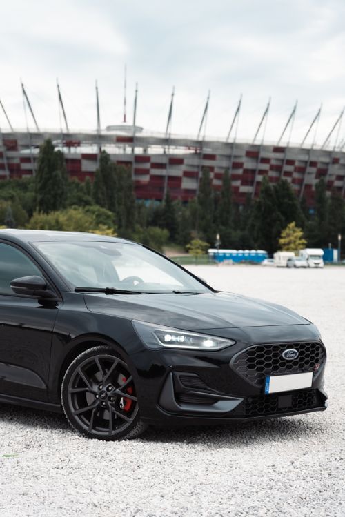 Free Sleek black car parked in front of a stadium during the day. Perfect for automotive themes. Stock Photo