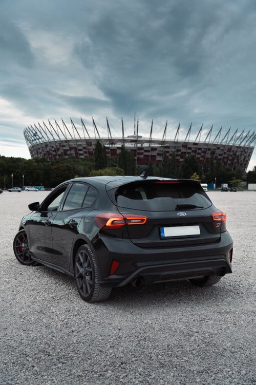 Free Black car parked in front of a modern stadium with overcast skies, highlighting unique architectural features. Stock Photo