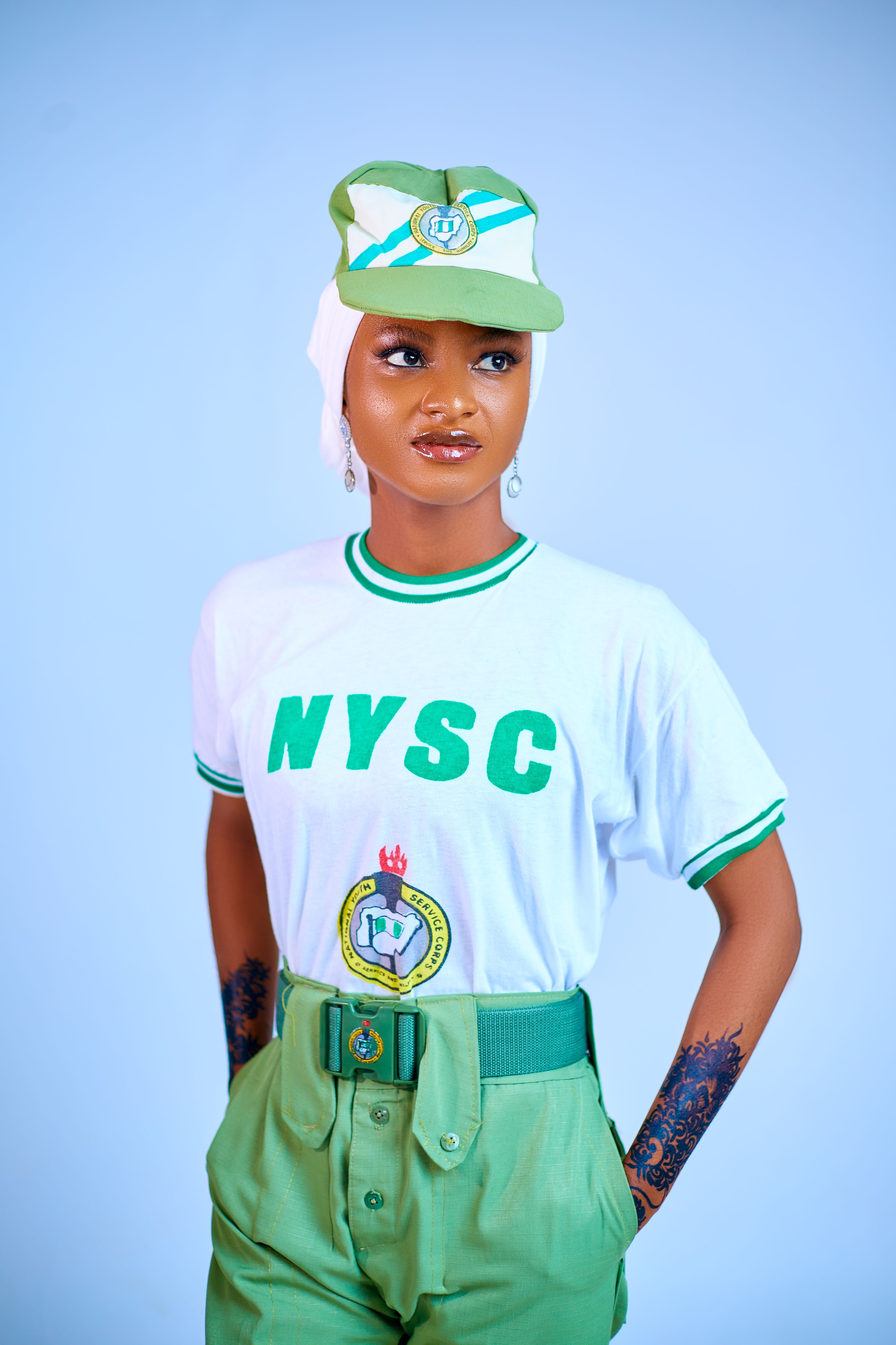 Confident young adult wearing NYSC uniform on blue background.