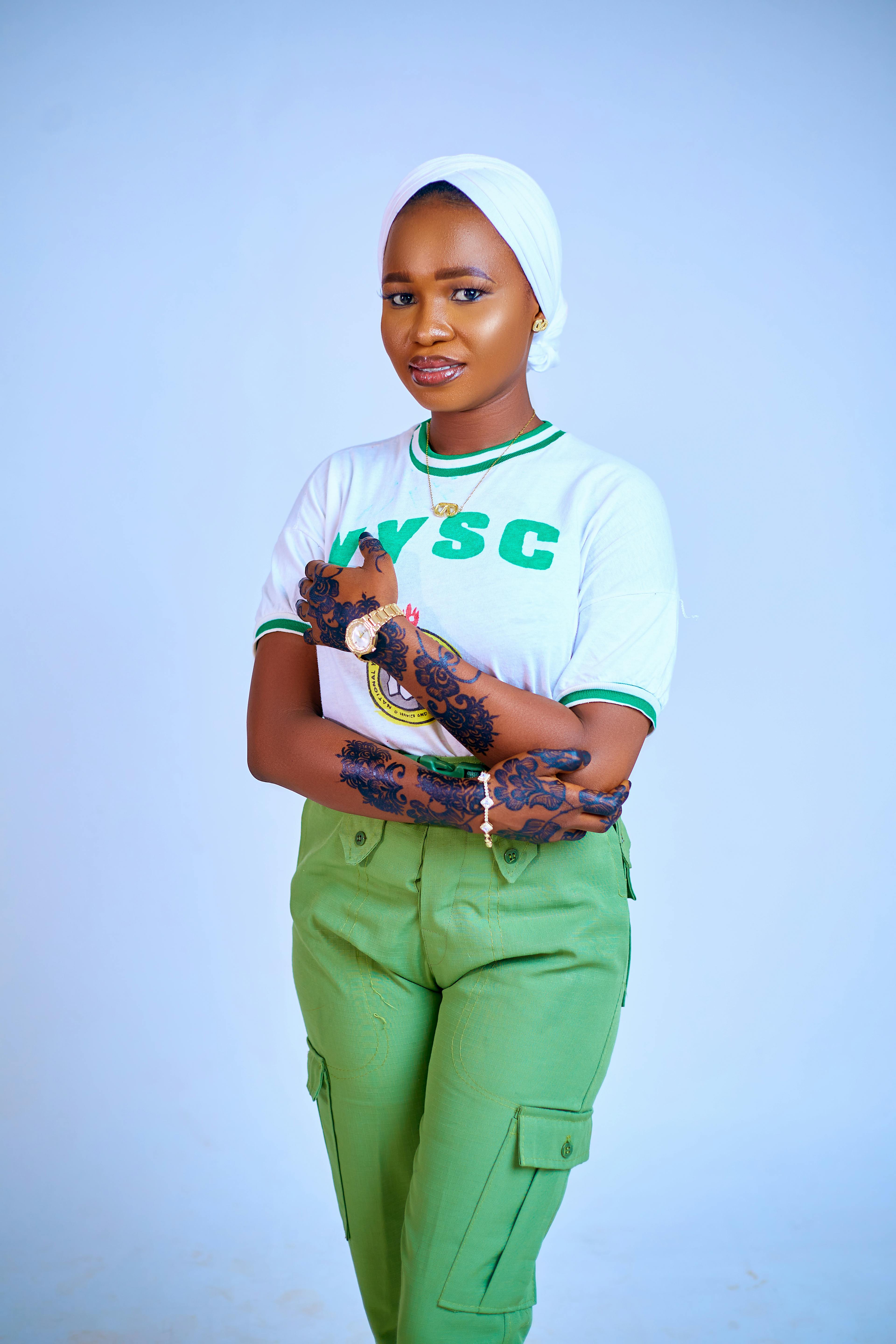Portrait of a woman in NYSC uniform with intricate henna design on hands.