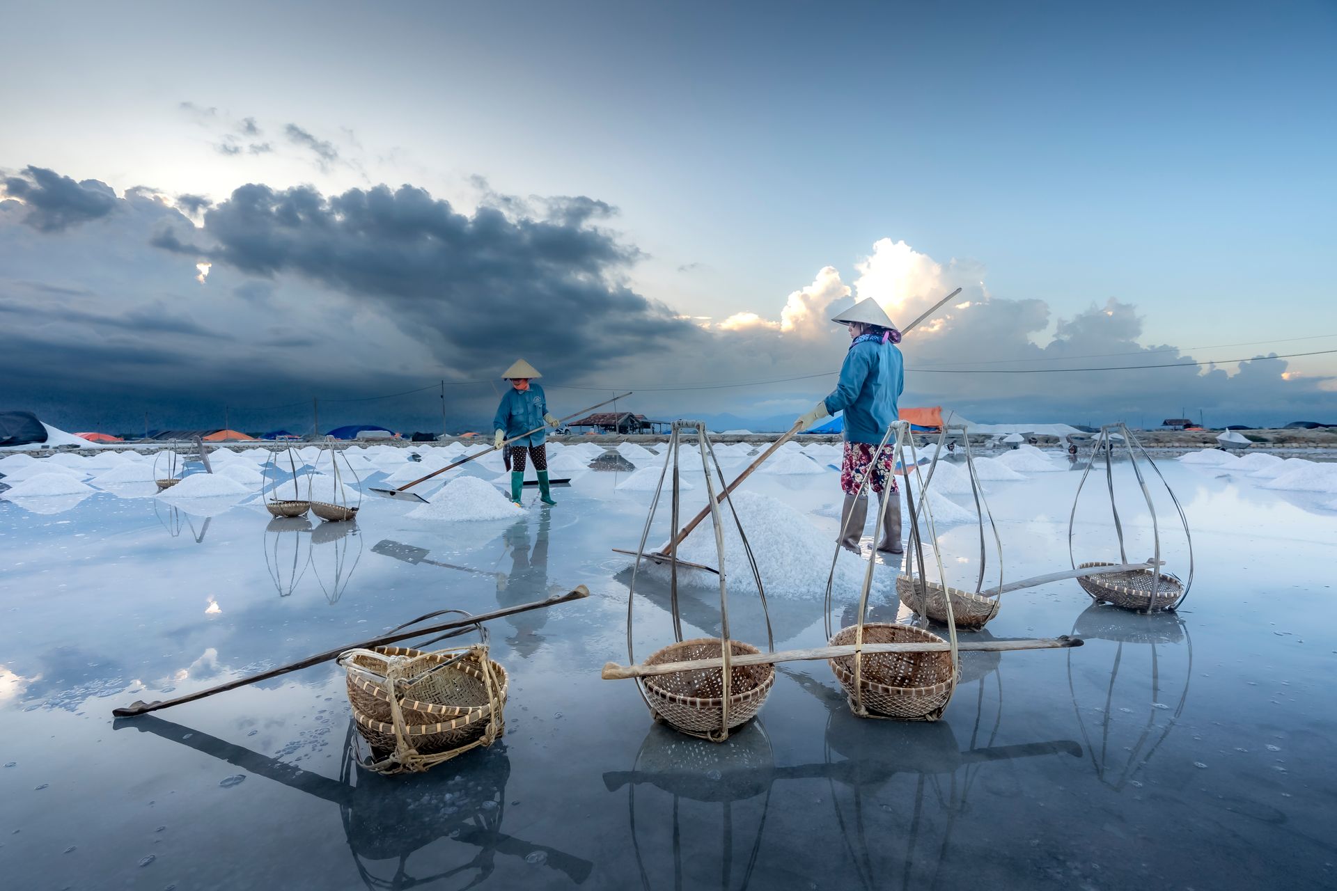 Salt farmers gathering salt on reflective water against a dramatic sky.