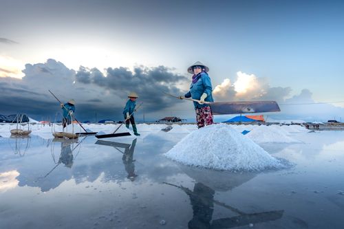 Free Farmers harvesting salt on reflective wetlands under dramatic sky, showcasing traditional methods. Stock Photo