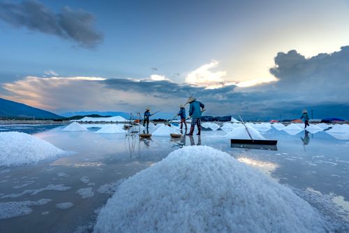 Free Workers gather salt from pools under a dramatic sky during dusk, creating a serene landscape. Stock Photo