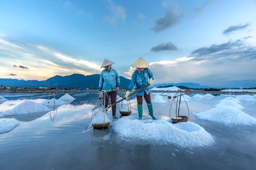 Free Two workers gather salt in Vietnam under a bright morning sky. Stock Photo