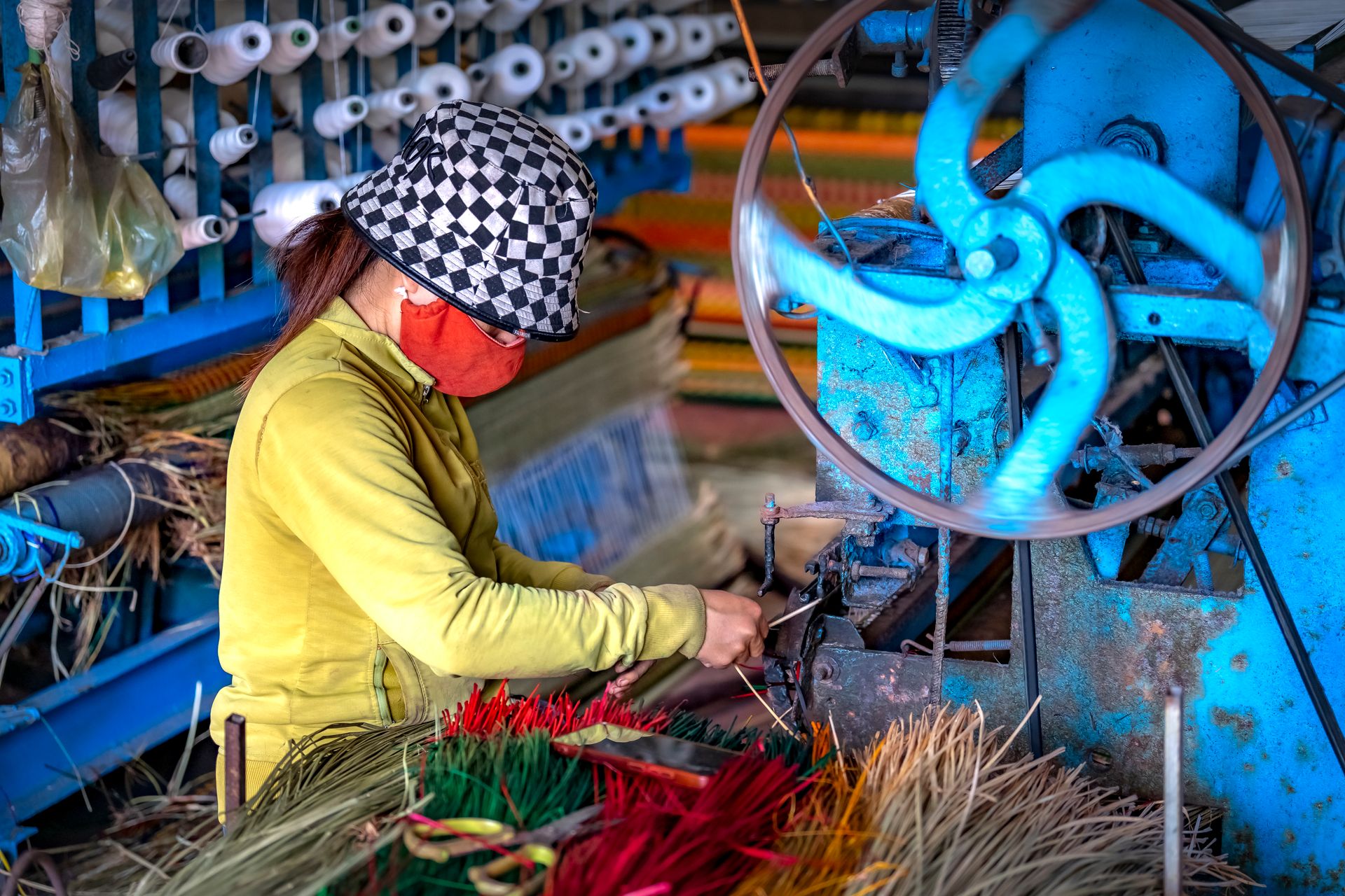 A worker in colorful attire operates a traditional weaving machine indoors, showcasing vibrant threads.