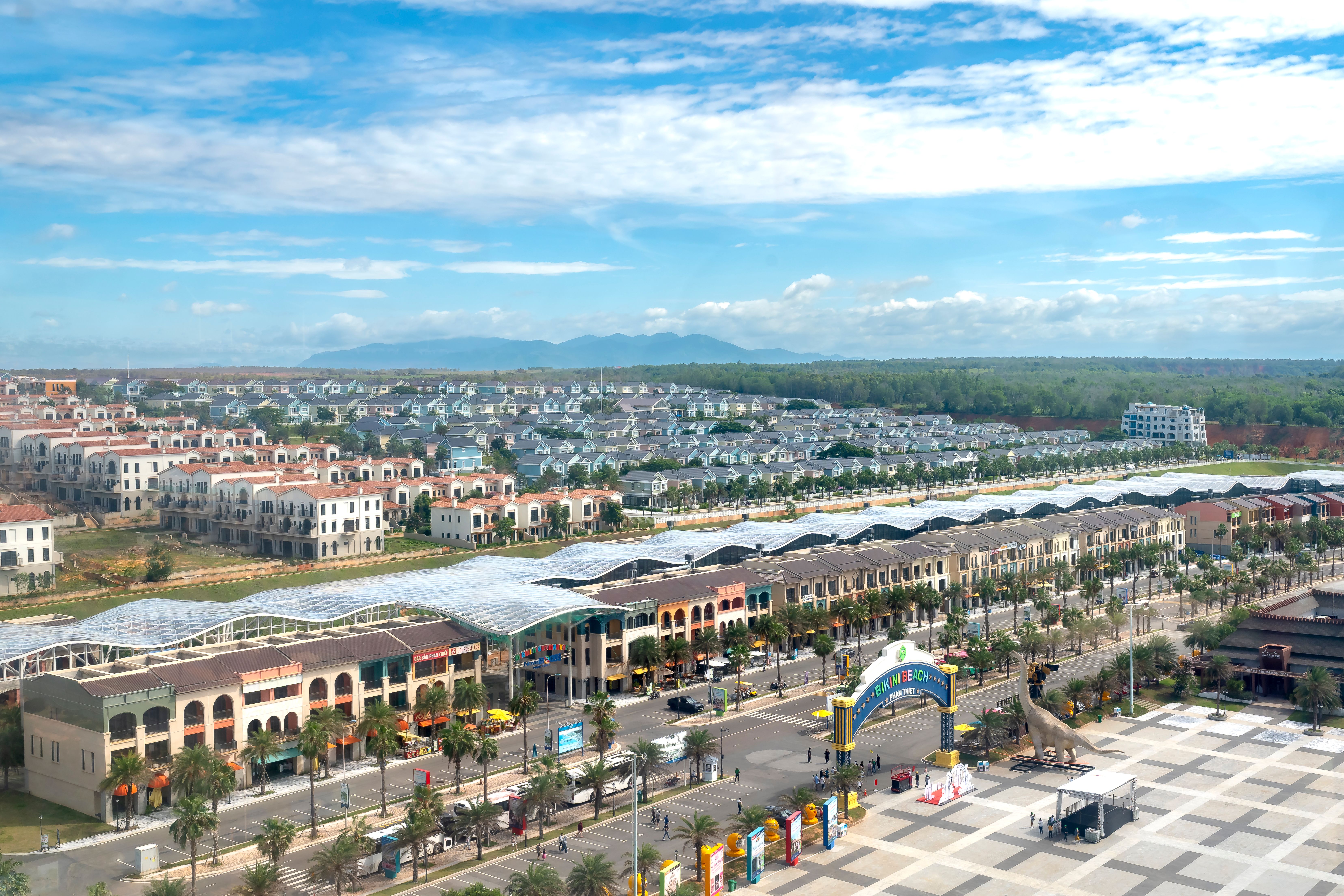 A vibrant aerial view of a cityscape with an amusement park entrance, palm trees, and blue sky.