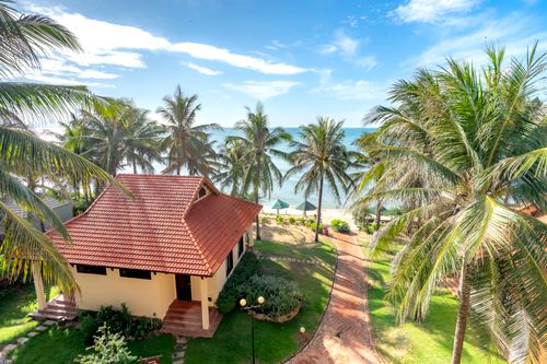 Free A serene tropical bungalow with palm trees overlooking the beach under a bright blue sky. Stock Photo