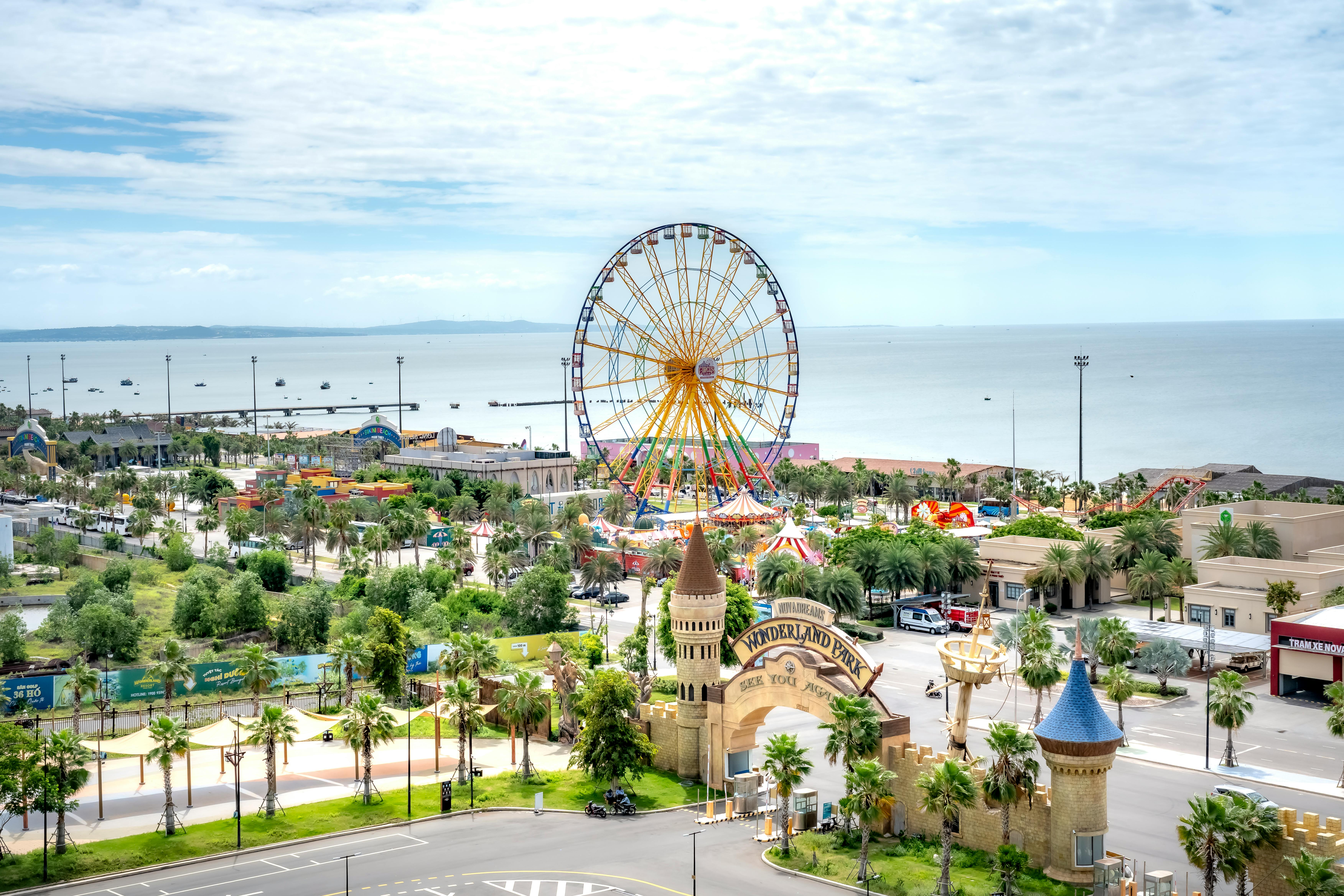 Bright aerial view of a coastal amusement park featuring a Ferris wheel and lush greenery.