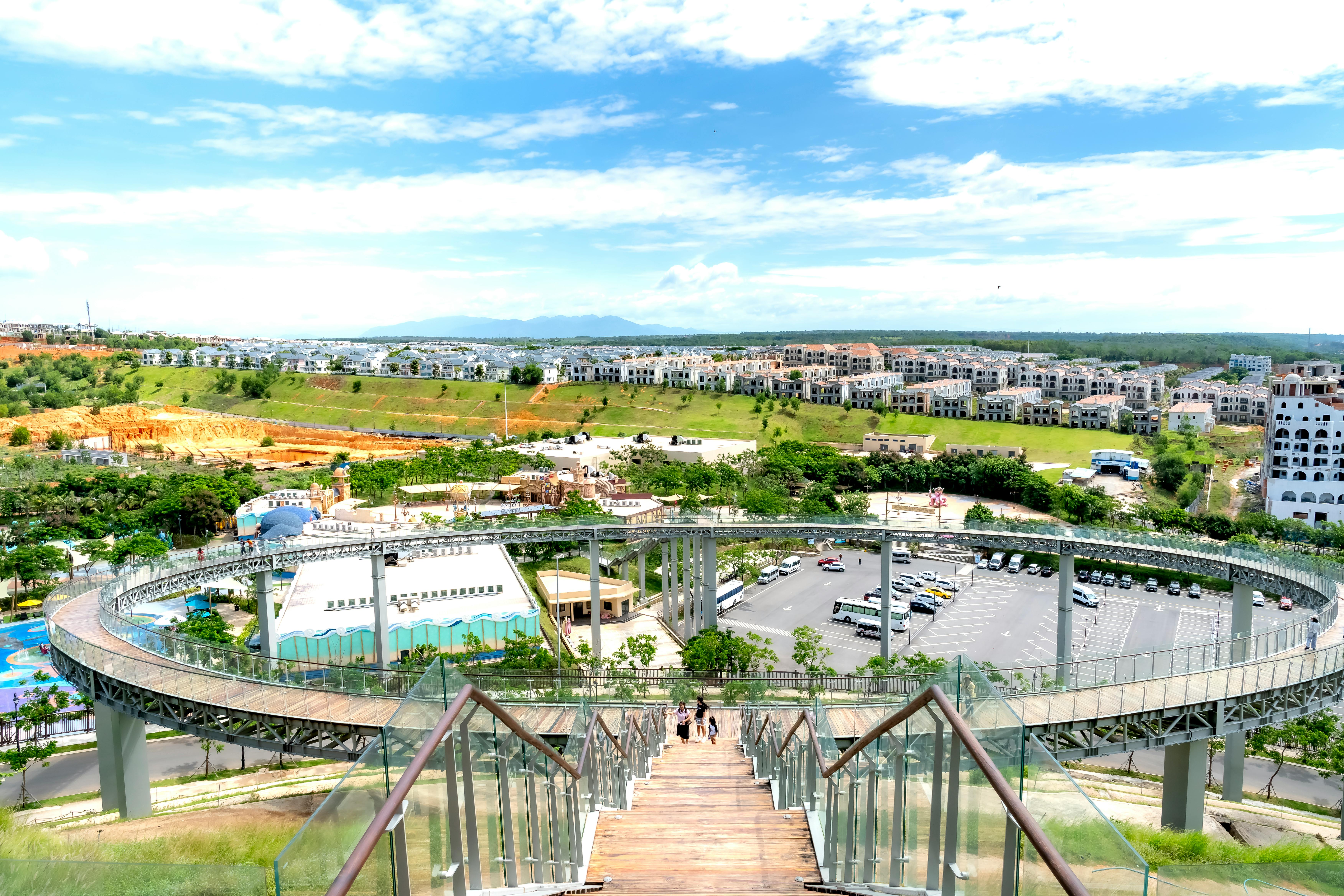 Aerial view of a modern park with a winding walkway and residential area in the distance.