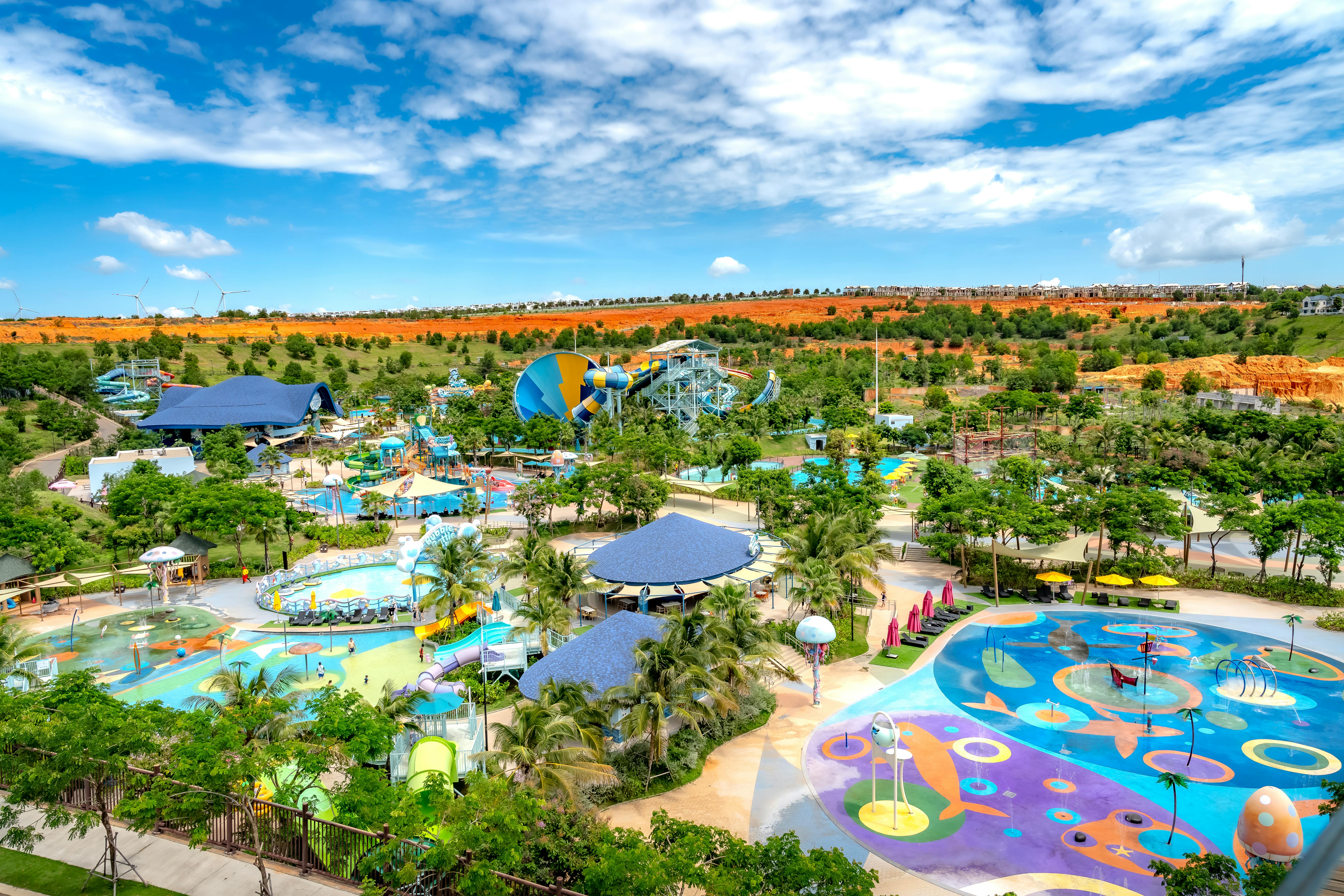Explore a colorful water park from above, showcasing slides, pools, and lush greenery under a bright summer sky.