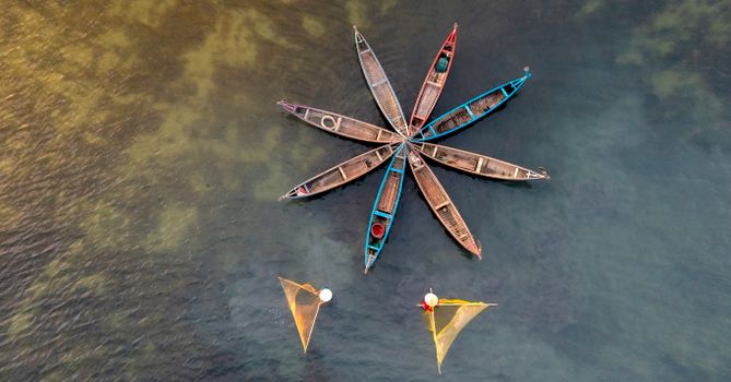 Aerial shot of boats arranged in a star shape on water with fishermen casting nets.