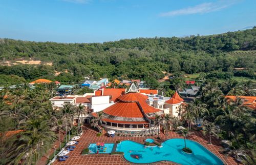 Free Aerial view of a tropical resort with a pool surrounded by greenery and vibrant architecture. Stock Photo