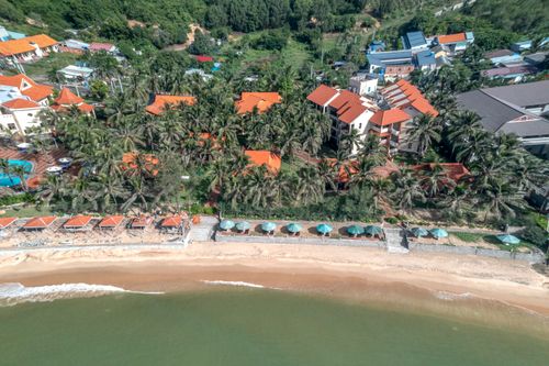 Free Sunny aerial shot of a beachfront resort with red roofs and palm trees lining the coast. Stock Photo