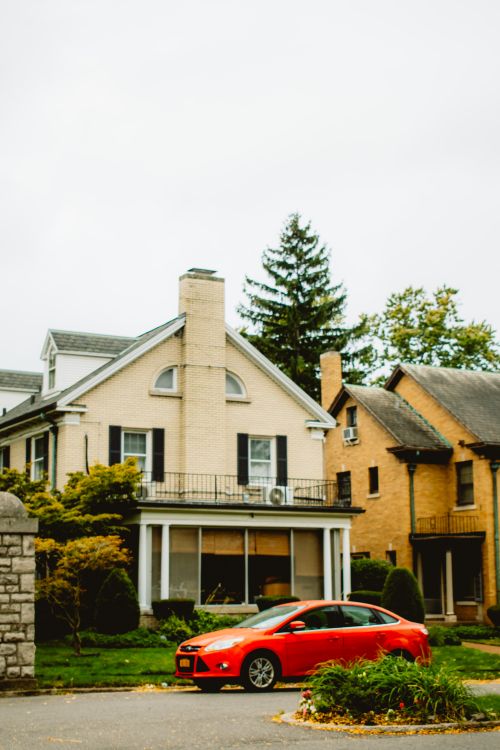 Free Charming suburban house with a vibrant red car parked in front, highlighting the cozy autumn atmosphere. Stock Photo
