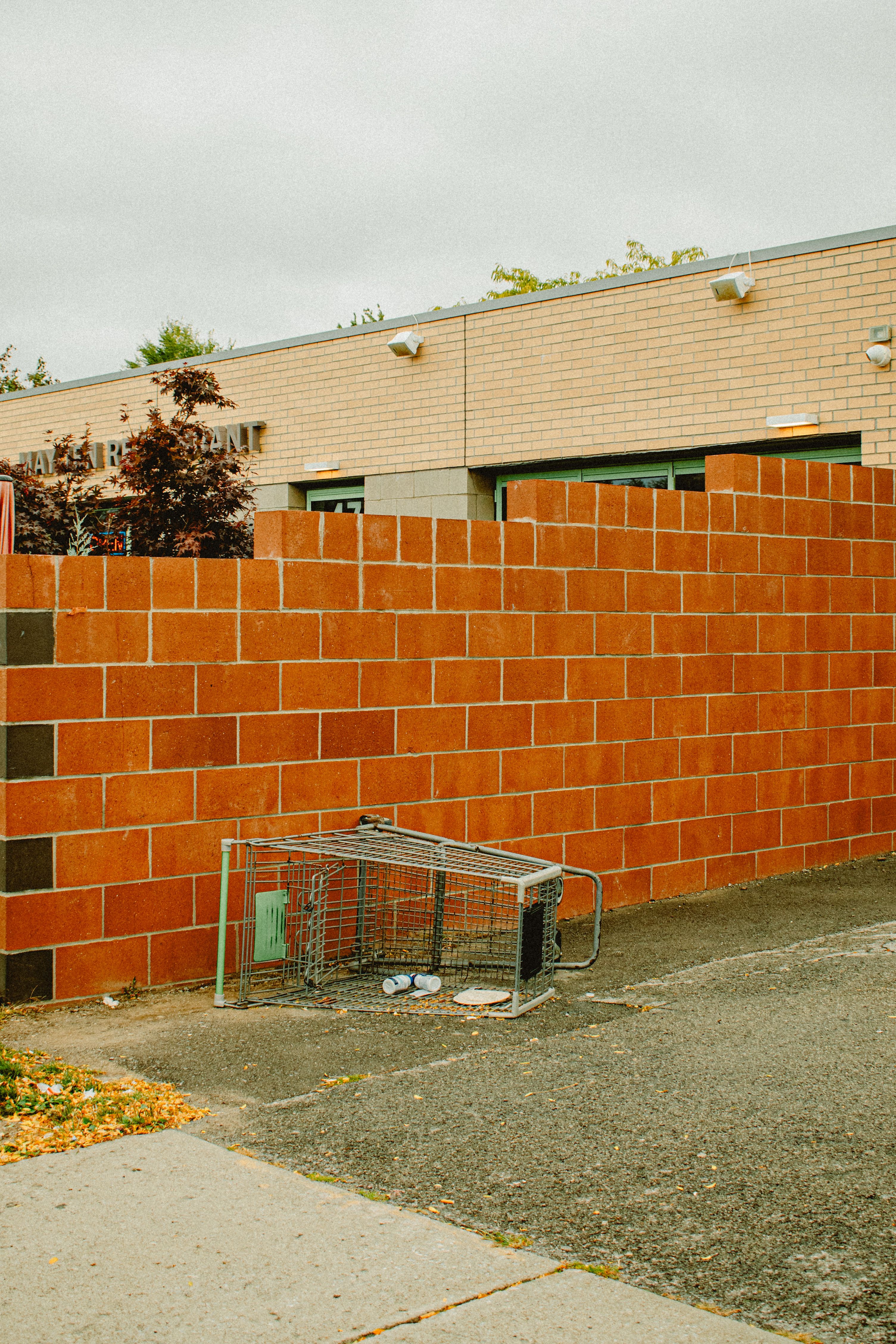 Abandoned shopping cart against a red brick wall outside a building.
