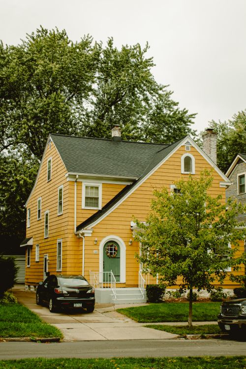 Free A charming yellow two-story house with a green door, car parked outside. Stock Photo