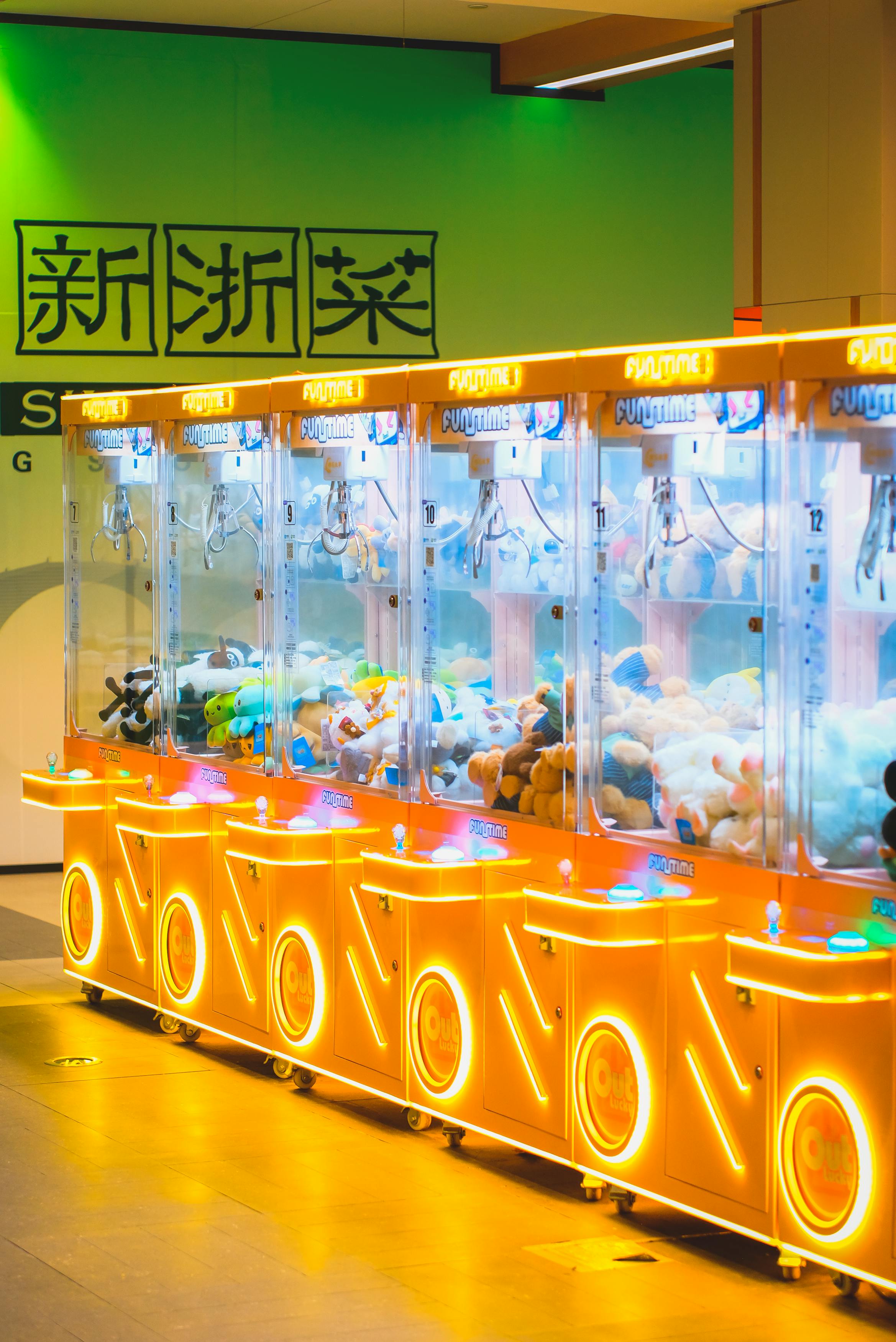 Bright row of claw machines filled with plush toys at an indoor arcade.