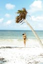 一名穿着比基尼的女子在热带海滩上奔跑，周围有倾斜的棕榈树和晴朗的蓝天