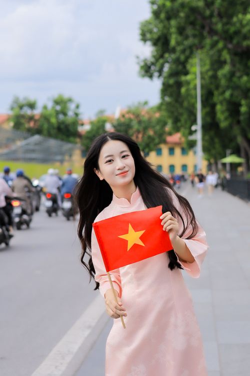 Free Smiling woman in pink dress holds Vietnamese flag on a busy street in Việt Nam. Stock Photo