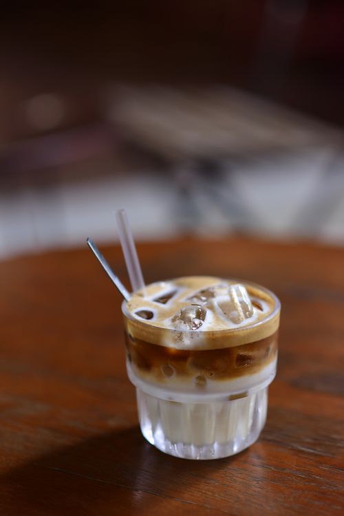Free A close-up of a refreshing iced coffee with cream in a glass on a rustic wooden table. Stock Photo