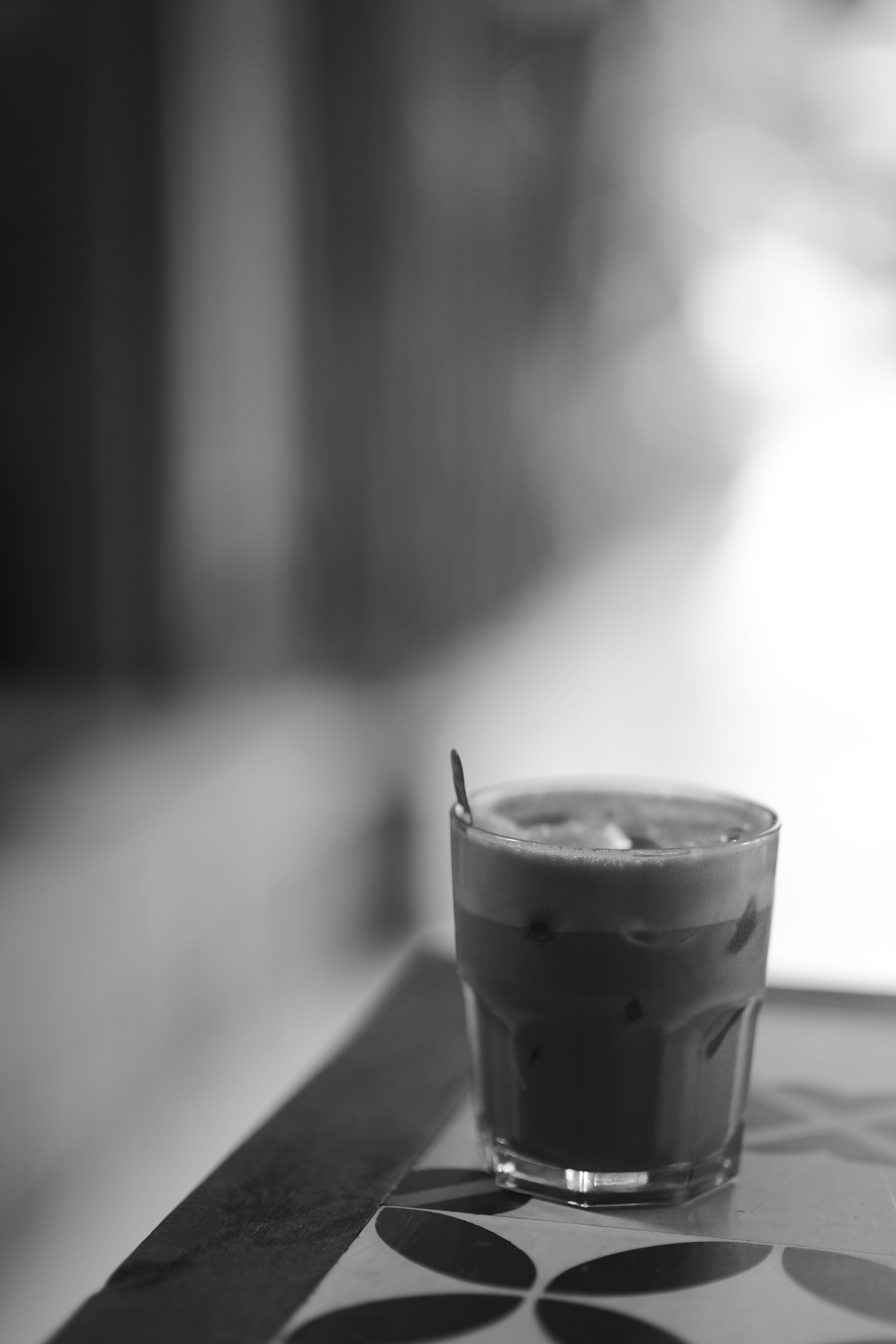 A black and white photo of a refreshing iced coffee placed on a patterned table, creating a moody ambiance.